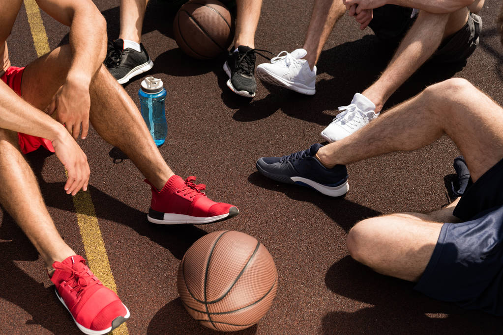 gedeeltelijke weergave van basketbal spelers met bal en sport fles zittend op basketbalveld - Foto, afbeelding