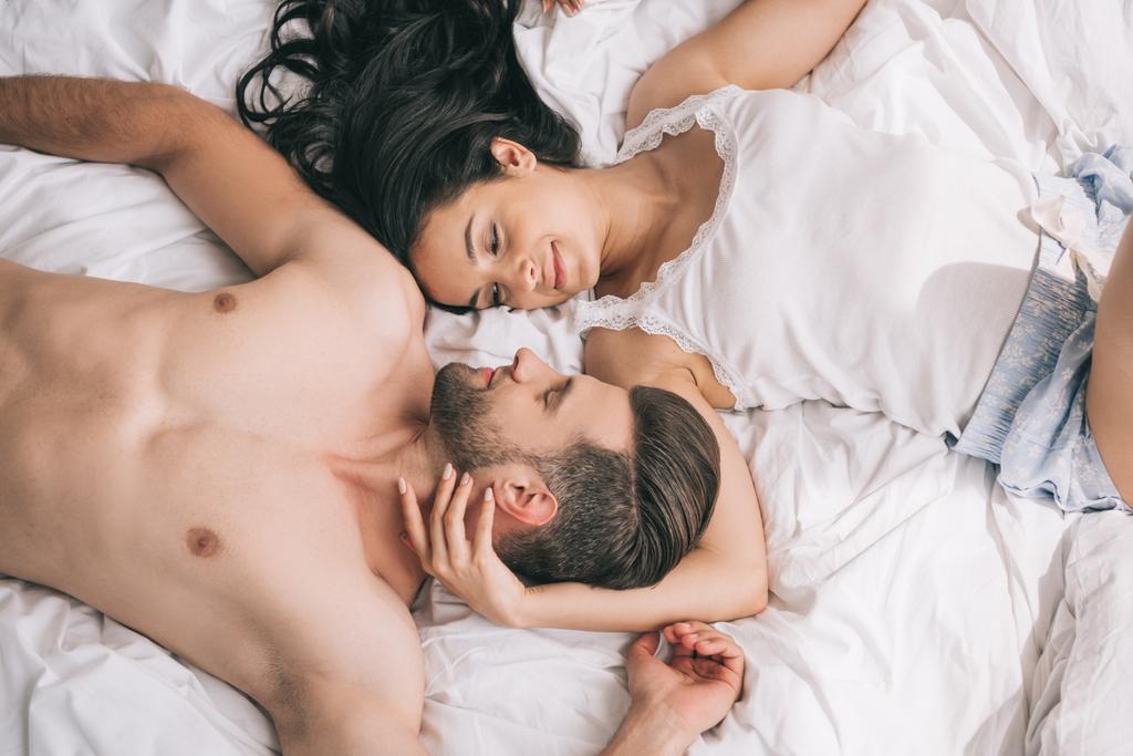 ylhäältä näkymä komea ja paidaton mies makaa houkutteleva nainen sängyssä
  - Valokuva, kuva