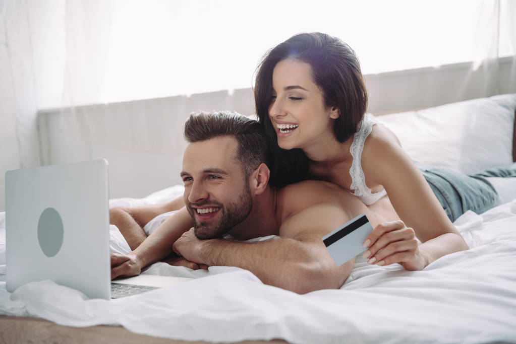 красива і усміхнена жінка тримає кредитну картку і красивого чоловіка за допомогою ноутбука
  - Фото, зображення