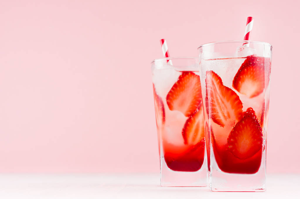 Cóctel de fresa fresca de verano con licor rojo, rodajas de bayas, cubitos de hielo y paja sobre fondo rosa pastel, espacio para copiar
. - Foto, imagen