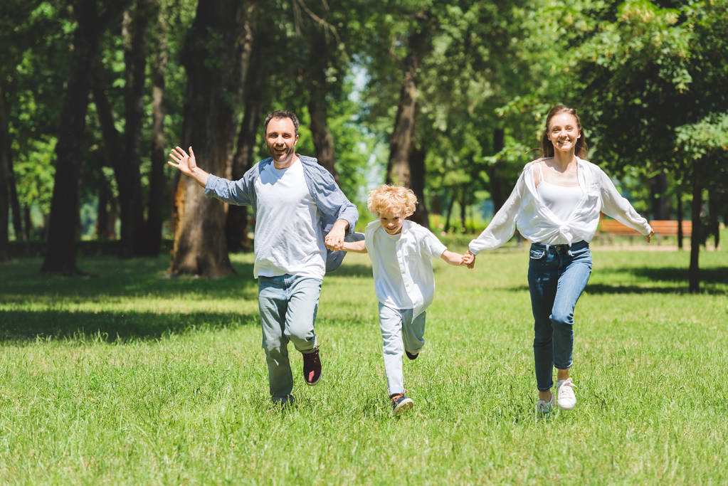 felice famiglia che si tiene per mano e corre nel parco durante il giorno
 - Foto, immagini