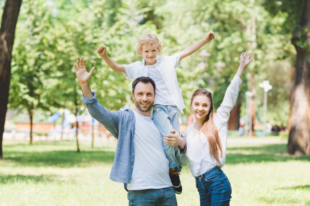 glückliche Familie mit ausgestreckten Händen, die im Park in die Kamera blickt - Foto, Bild