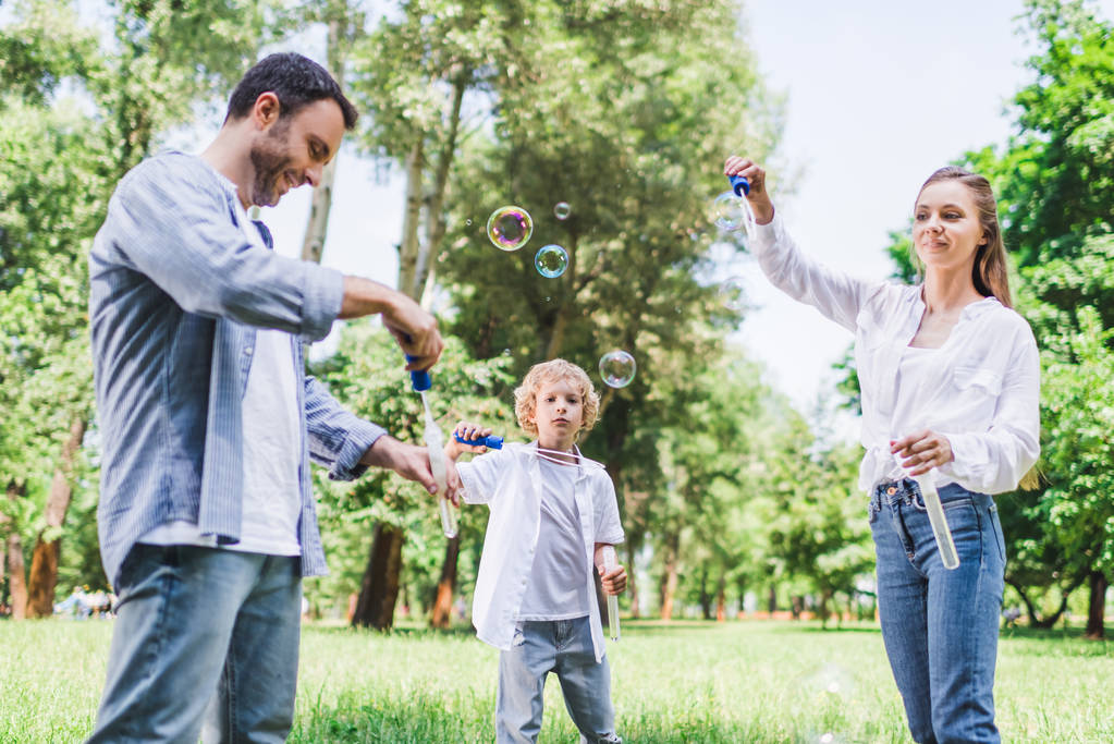 красивая мать, отец и сын играют с мыльными пузырями в парке
 - Фото, изображение