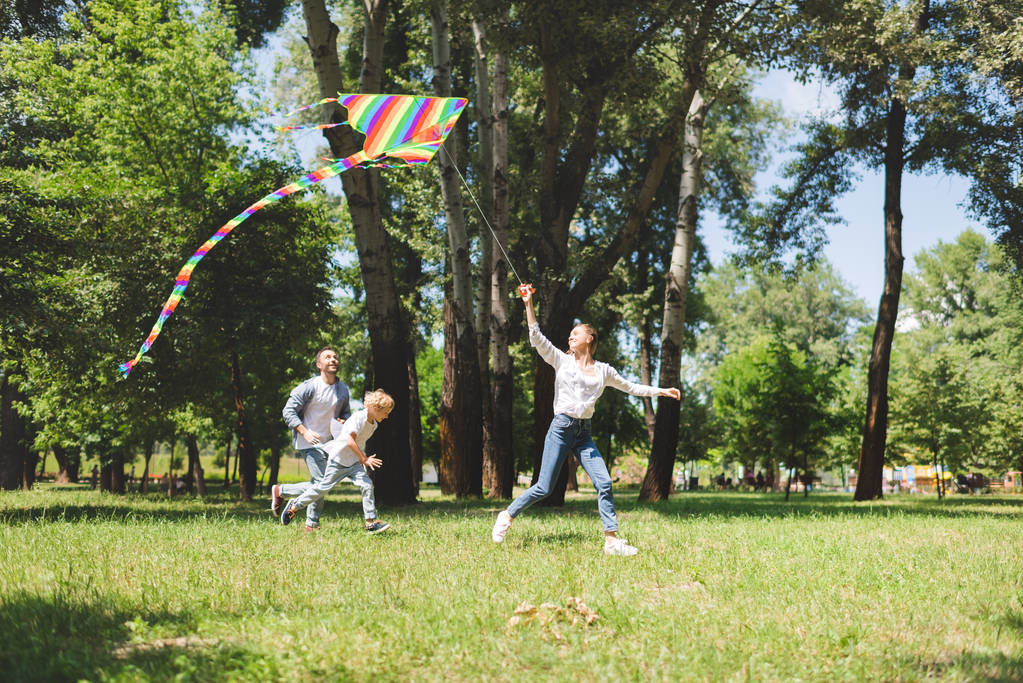excited family running and playing with flying kite in park - Photo, Image