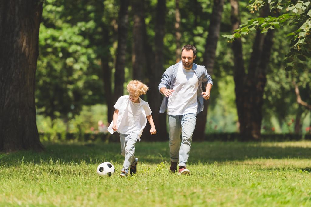 Ojciec i godny podziwu syn gra w piłka nożna w Park razem  - Zdjęcie, obraz