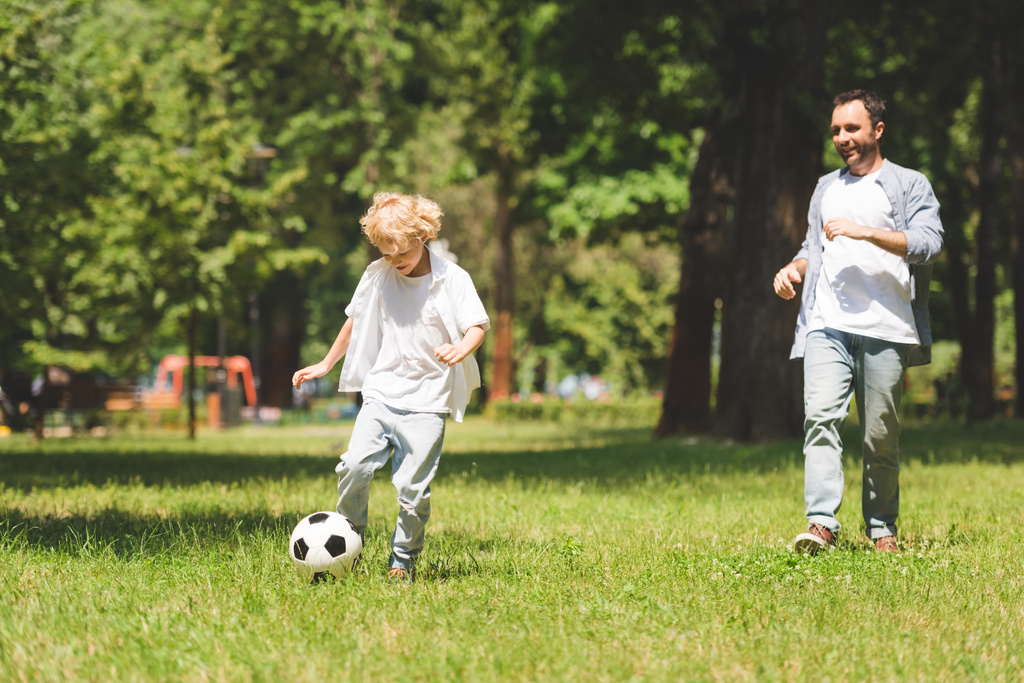 Vater und entzückender Sohn spielen tagsüber Fußball im Park - Foto, Bild