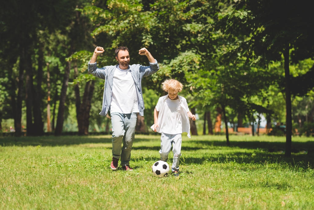 Aufgeregter Vater und entzückender Sohn spielen Fußball im Park - Foto, Bild