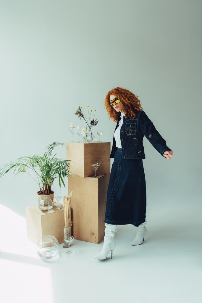fille rousse à la mode posant près des boîtes en bois, des lunettes et des plantes sur gris
 - Photo, image