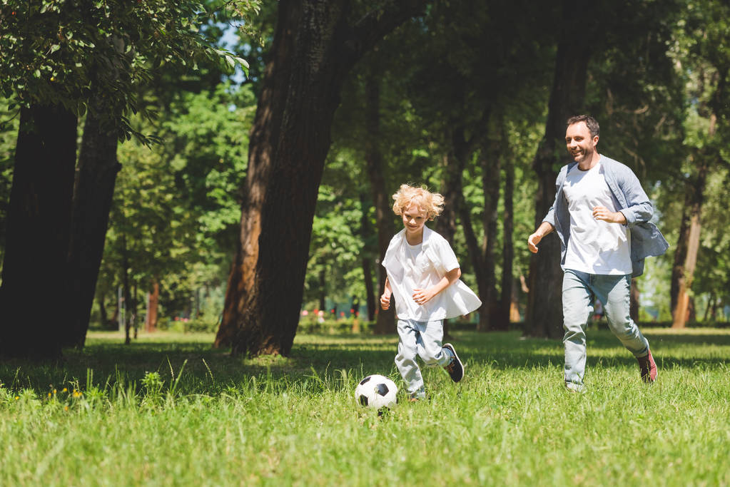πατέρας και αξιολάτρευτο γιο παίζοντας ποδόσφαιρο με μπάλα ποδοσφαίρου στο πάρκο με χώρο αντιγραφής - Φωτογραφία, εικόνα