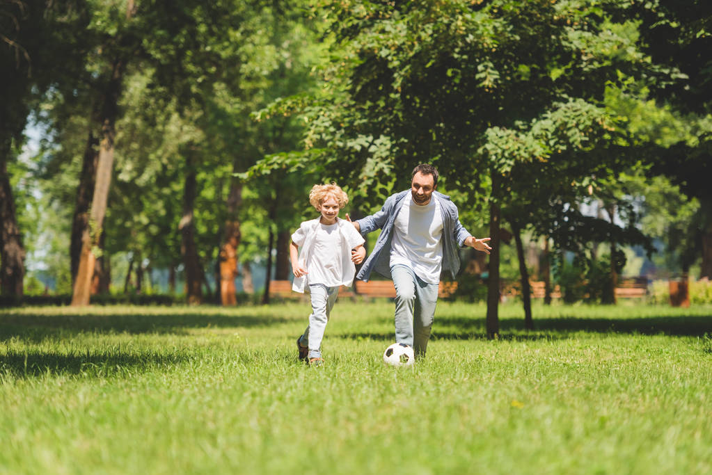 отец и очаровательный сын играют в футбол с футбольным мячом в парке
 - Фото, изображение