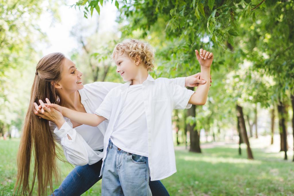 beautiful happy mother holding hands with adorable son in park - Photo, Image
