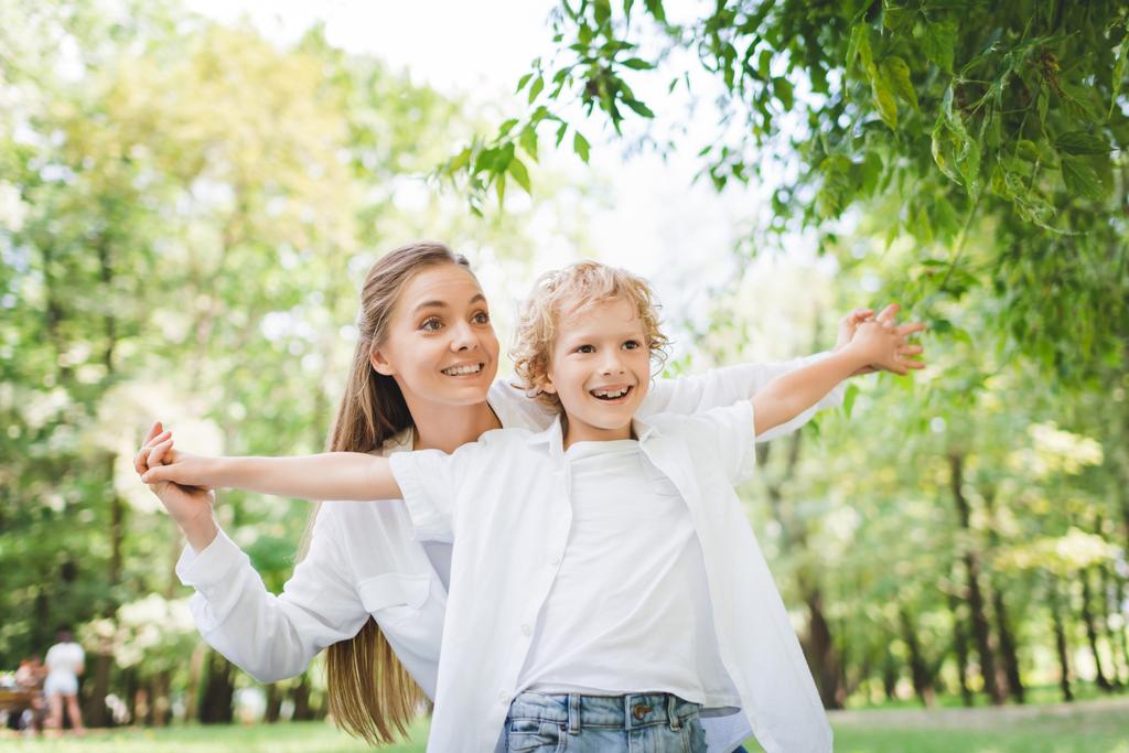 piękna szczęśliwa matka trzyma ręce z uroczym synem w parku - Zdjęcie, obraz