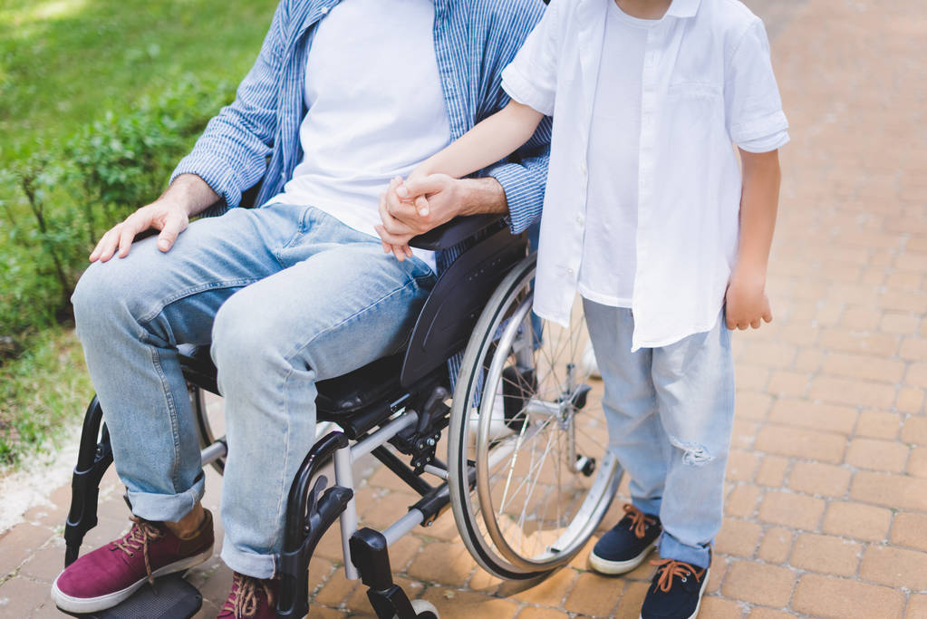 przycięte widok syna hloding ręce z niepełnosprawnym ojcem na wózku inwalidzkim - Zdjęcie, obraz