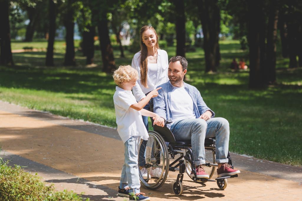 kaunis äiti ja poika vammainen isä pyörätuolilla puistossa
 - Valokuva, kuva