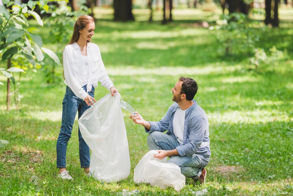 man and woman picking up garbage in plastic bags in park - Photo, Image