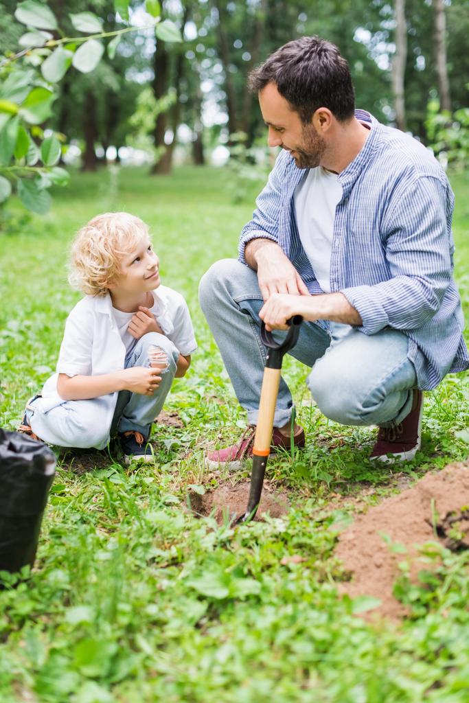 father and cute son during digging ground with shovel for planting seedling in park - Photo, Image