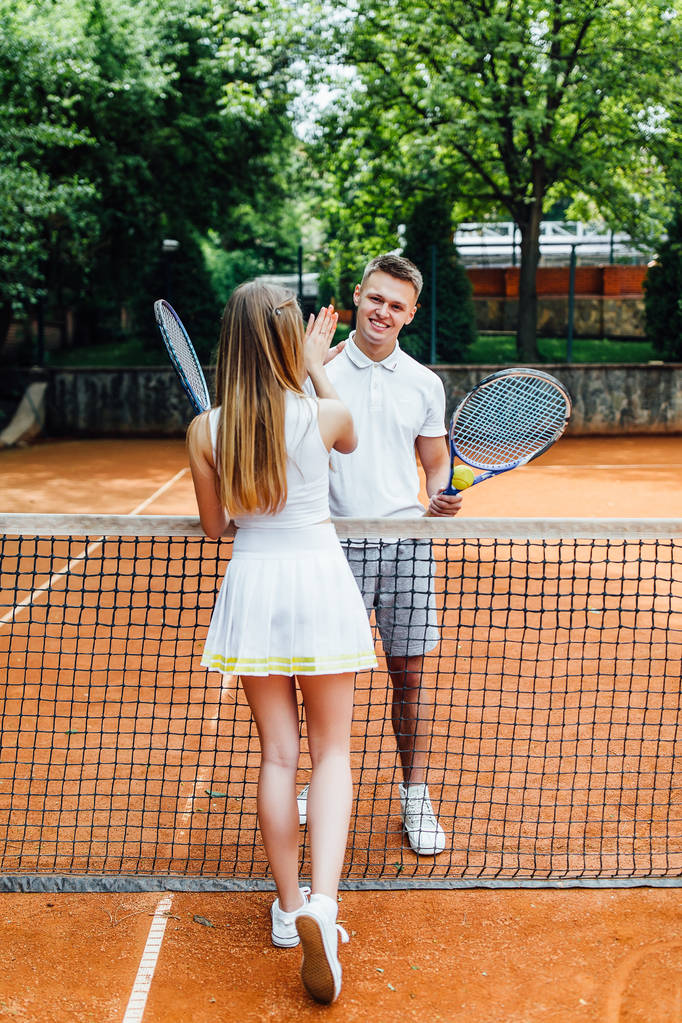 Knappe man en aantrekkelijke vrouw geven vijf, na klaar met het spelen van tennis - Foto, afbeelding