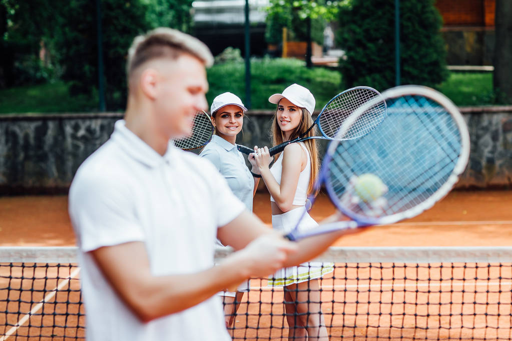 Férfi lengő tenisz ütő két lány mögött  - Fotó, kép