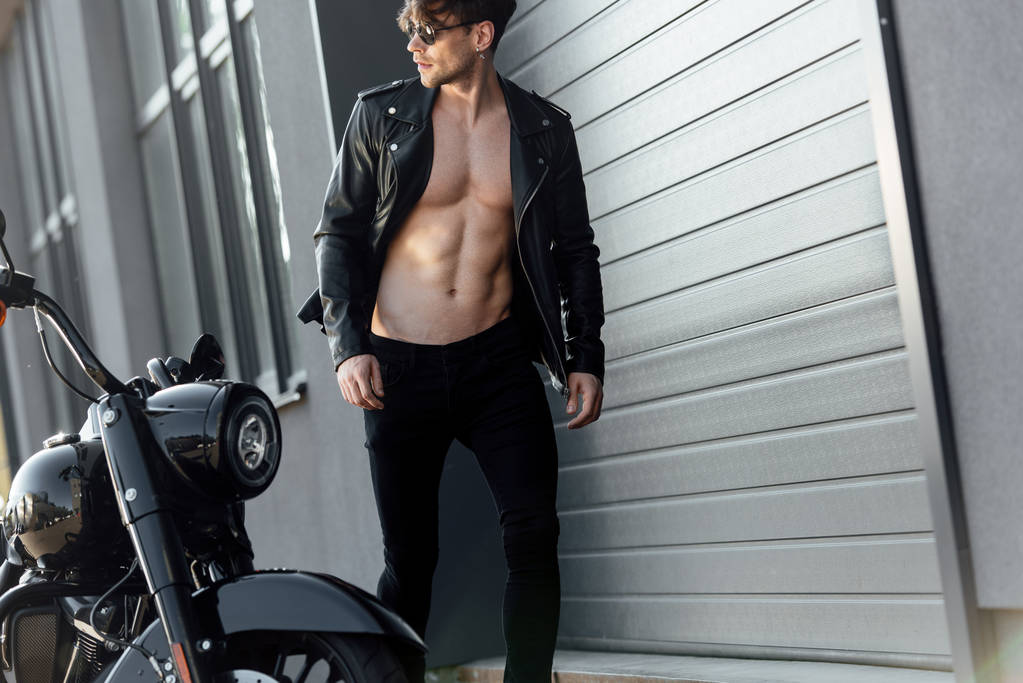 オートバイの近くを歩くヌード筋肉の胴体を持つ若い男 - 写真・画像