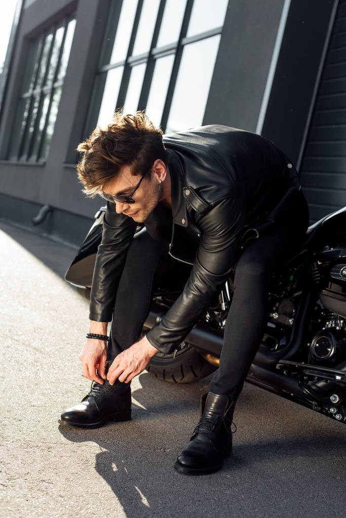 young man lacing up boots while sitting on black motorcycle - Photo, Image