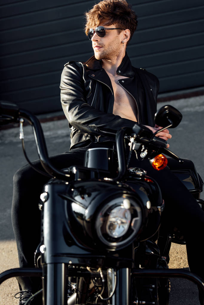без сорочки красивий молодий чоловік у шкіряній куртці відпочиває на чорному мотоциклі
 - Фото, зображення