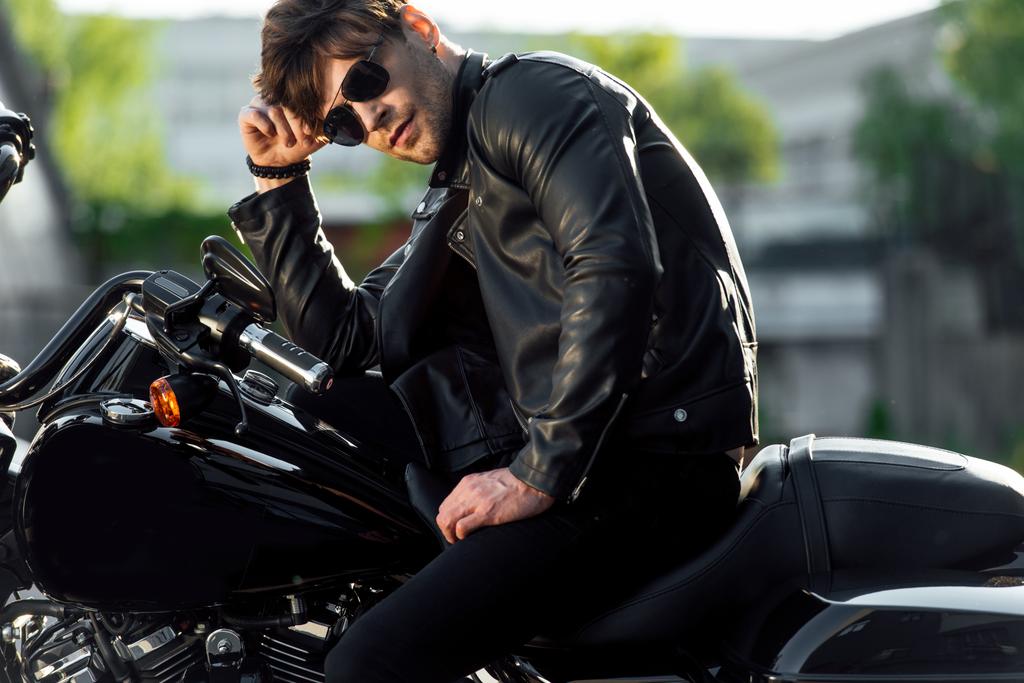 полный вид на мотоциклиста без рубашки, стоящего рядом с мотоциклом снаружи и смотрящего в сторону
 - Фото, изображение