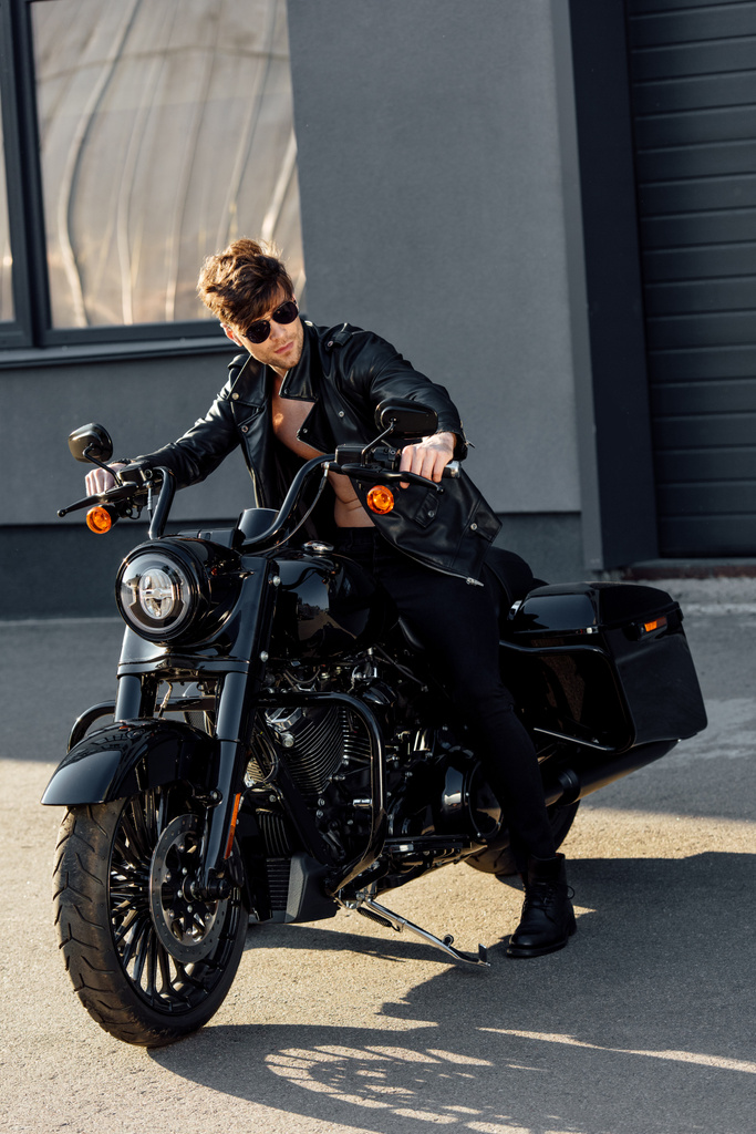 visão de comprimento total do motociclista em jaqueta de couro preto e óculos de sol sentados na motocicleta
 - Foto, Imagem