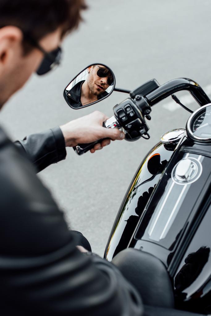 selektivní zaměření reflexe hezkého mladého muže v paprpakách sedícího na motocyklu - Fotografie, Obrázek