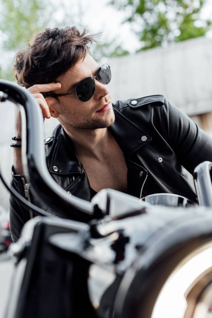 selektivní zaměření pohledného muže na sluneční brýle sedícího na motocyklu a s pohledem ven - Fotografie, Obrázek