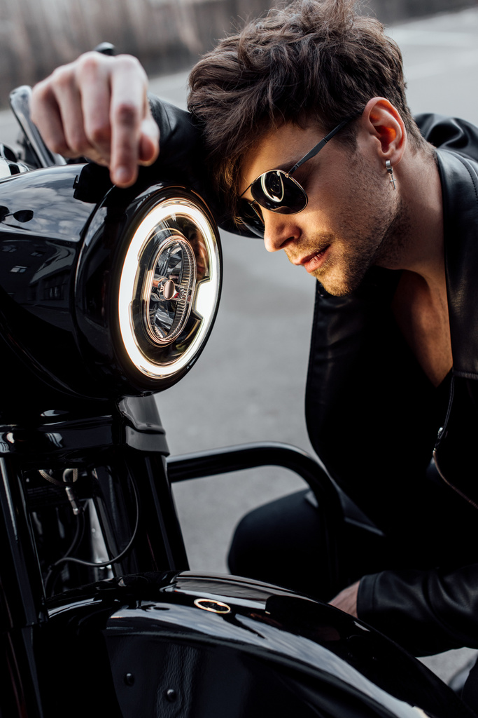 όμορφος νέος άντρας με γυαλιά ηλίου που γέρνει σε φωτεινή λάμπα στη μοτοσικλέτα - Φωτογραφία, εικόνα