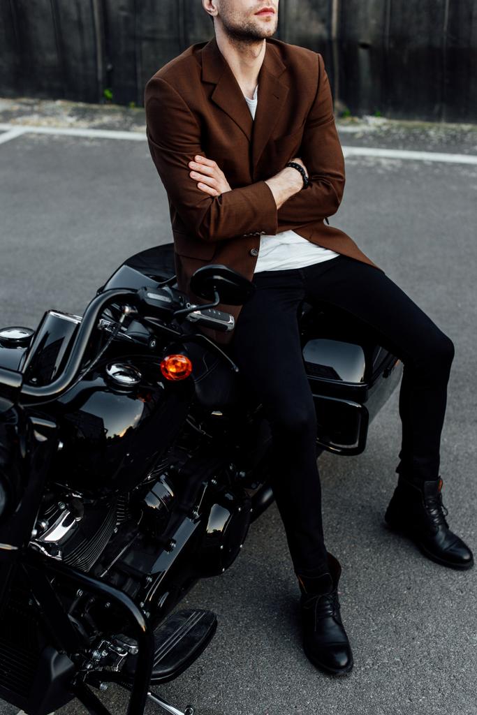 cropped view of man in jacket with crossed arms sitting on black motorcycle  - Photo, Image