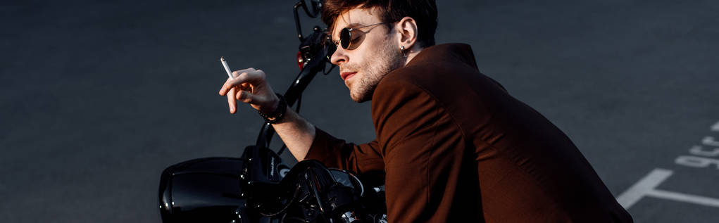панорамный снимок молодого человека, сидящего на мотоцикле и курящего сигарету
 - Фото, изображение