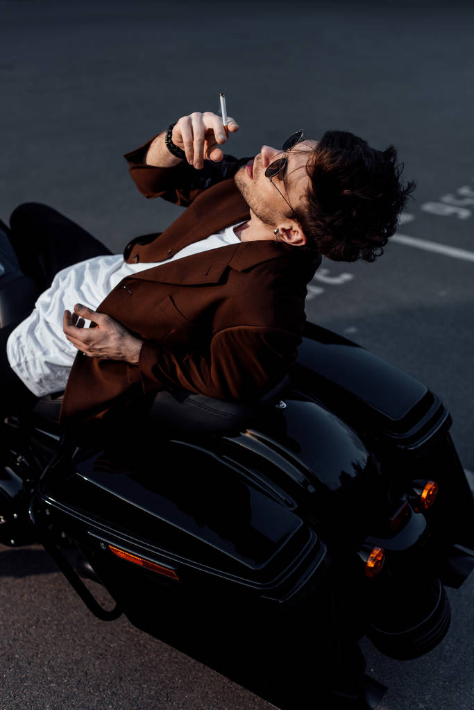 νέος άντρας που αναπαύεται σε μοτοσικλέτα και κάπνισμα τσιγάρων - Φωτογραφία, εικόνα