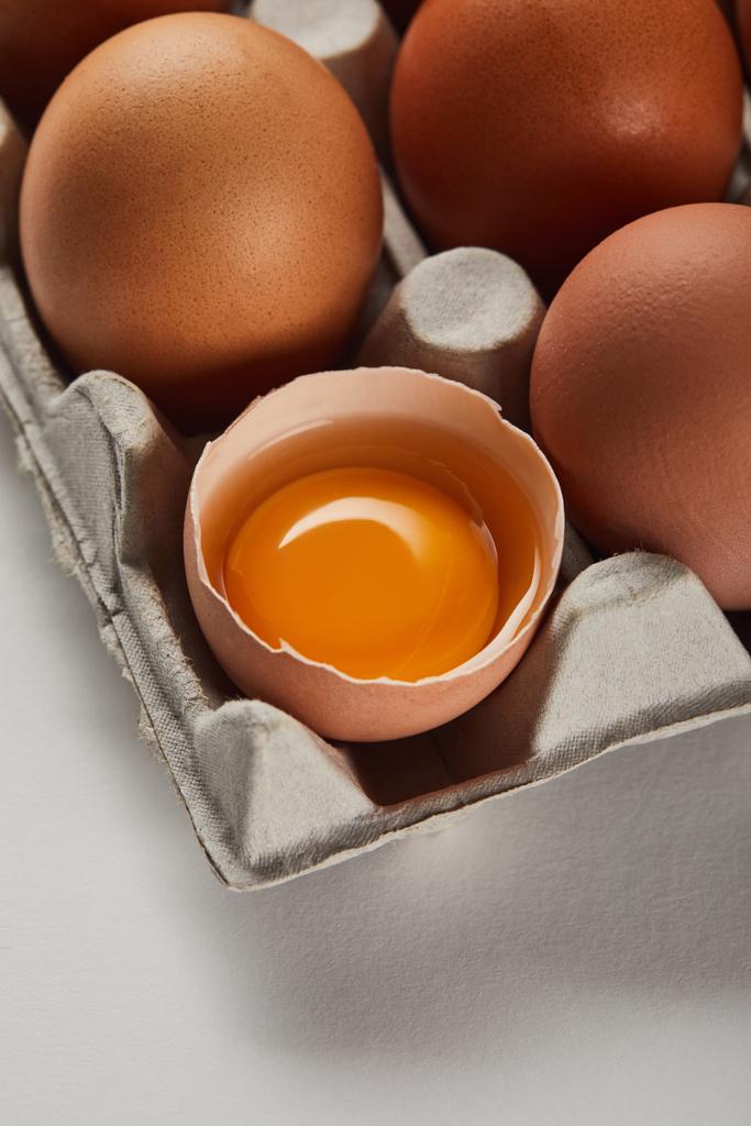 Zerbrochene Eierschale mit gelbem Eigelb in der Nähe von Eiern im Karton - Foto, Bild