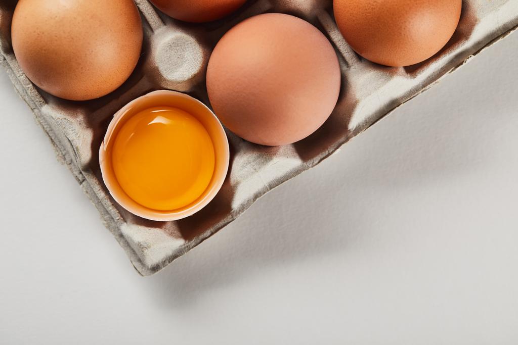  верхний вид сломанной яичной скорлупы с желтком рядом с яйцами в коробке
 - Фото, изображение