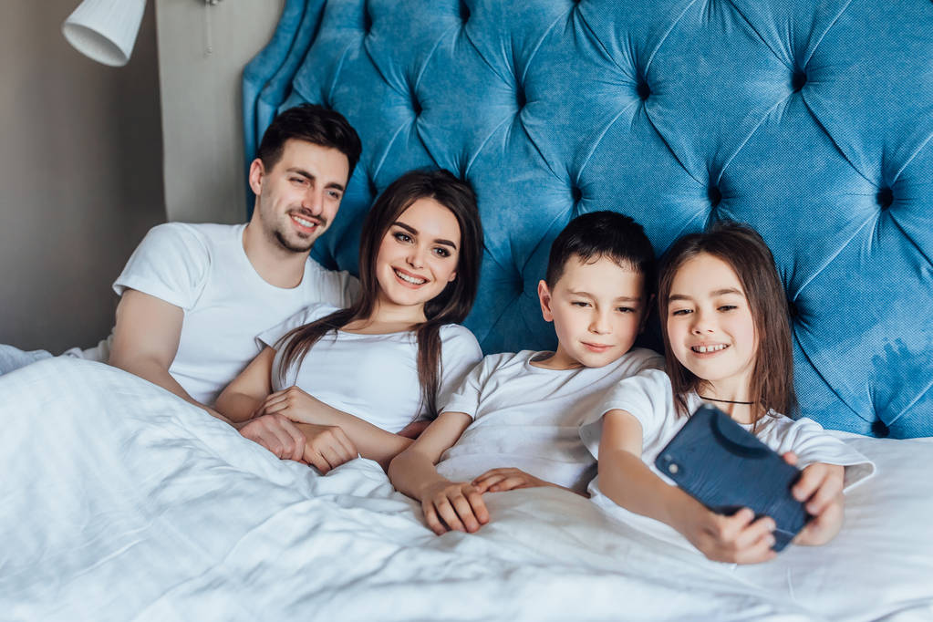 perhe viettää aikaa yhdessä sängyssä kotona
   - Valokuva, kuva