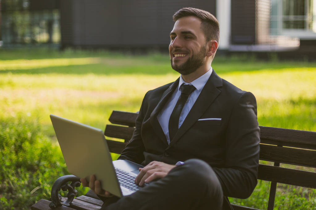 Елегантний бізнесмен, який використовує ноутбук, сидячи на відкритому повітрі. Телефоноване зображення
. - Фото, зображення