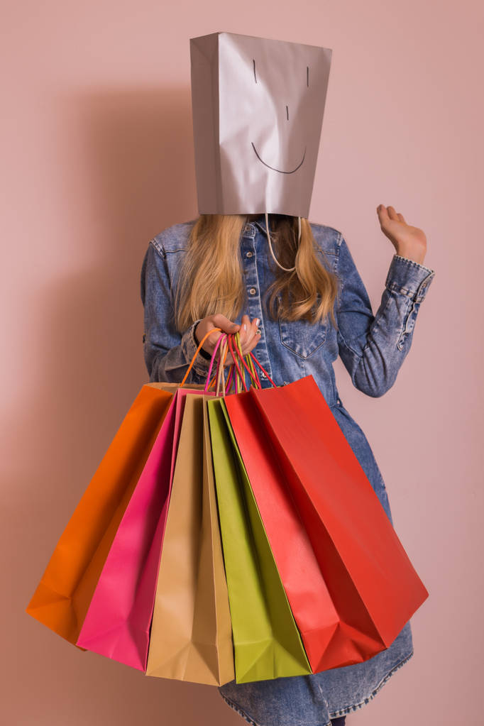 Παιχνιδιάρικη γυναίκα κρατώντας σακούλες αγορών με τσάντα στο κεφάλι της, ενώ στέκεται μπροστά από τον τοίχο. - Φωτογραφία, εικόνα