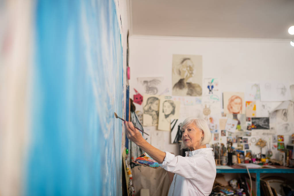 Femme portant une blouse blanche coloriant la toile en couleur bleue
 - Photo, image