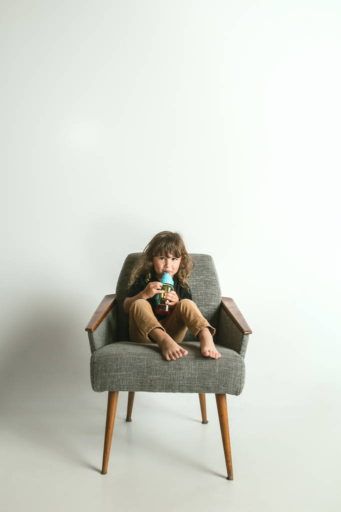 Маленька дитина сидить і грає в кріслі на білому фоні студії
 - Фото, зображення