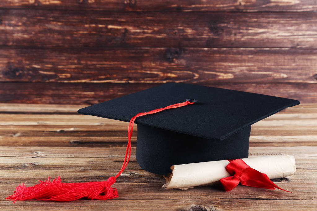 Graduation cap met diploma op bruin houten tafel - Foto, afbeelding