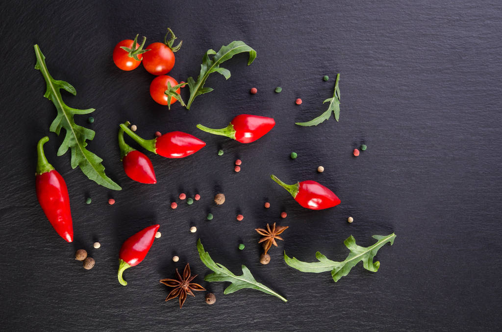Verschiedene Gewürze mit Tomate und Paprika auf schwarzem Hintergrund - Foto, Bild