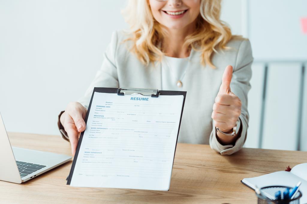 cropped view of woman holding clipboard with resume lettering and showing thumb up  - Photo, Image