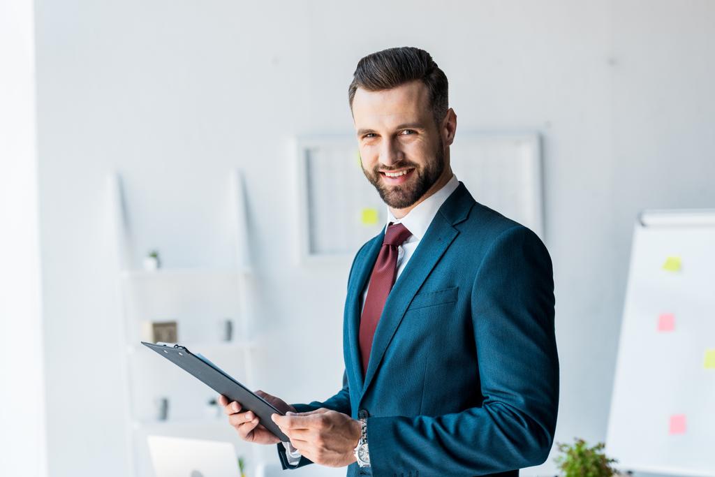 Veselý vousatý muž v obleku, který drží schránku v kanceláři  - Fotografie, Obrázek