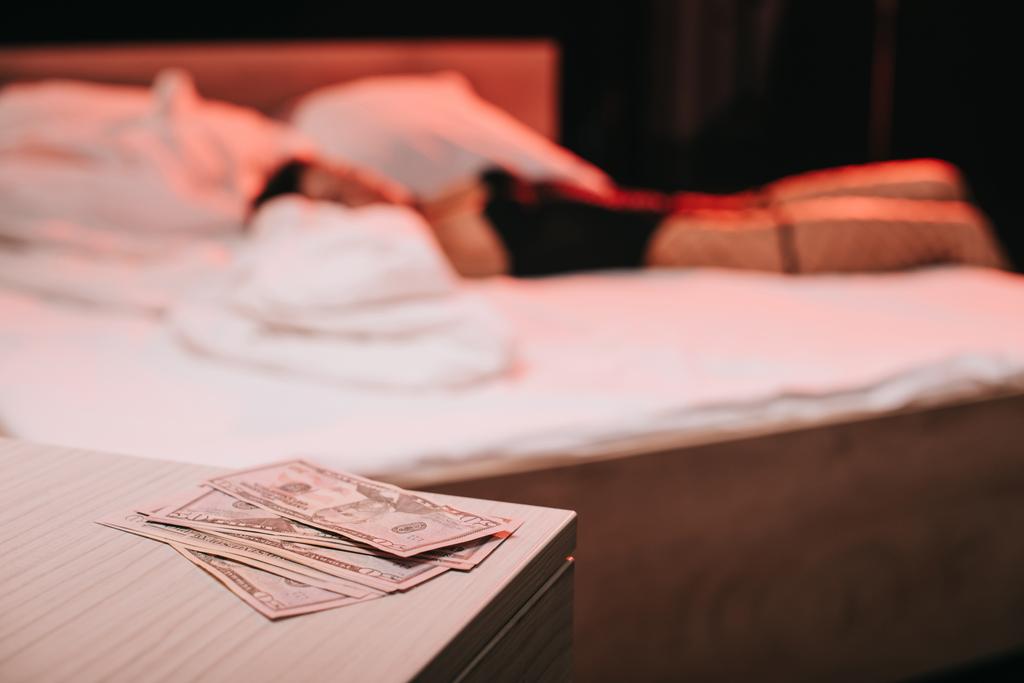 enfoque selectivo de billetes de dólar en la mesita de noche cerca de la mujer en la cama
  - Foto, Imagen