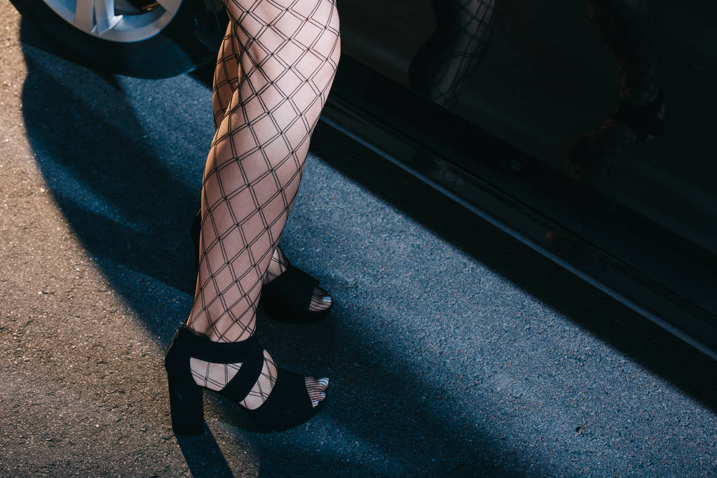 cropped view of woman in mesh stockings standing in shoes near car  - Photo, Image