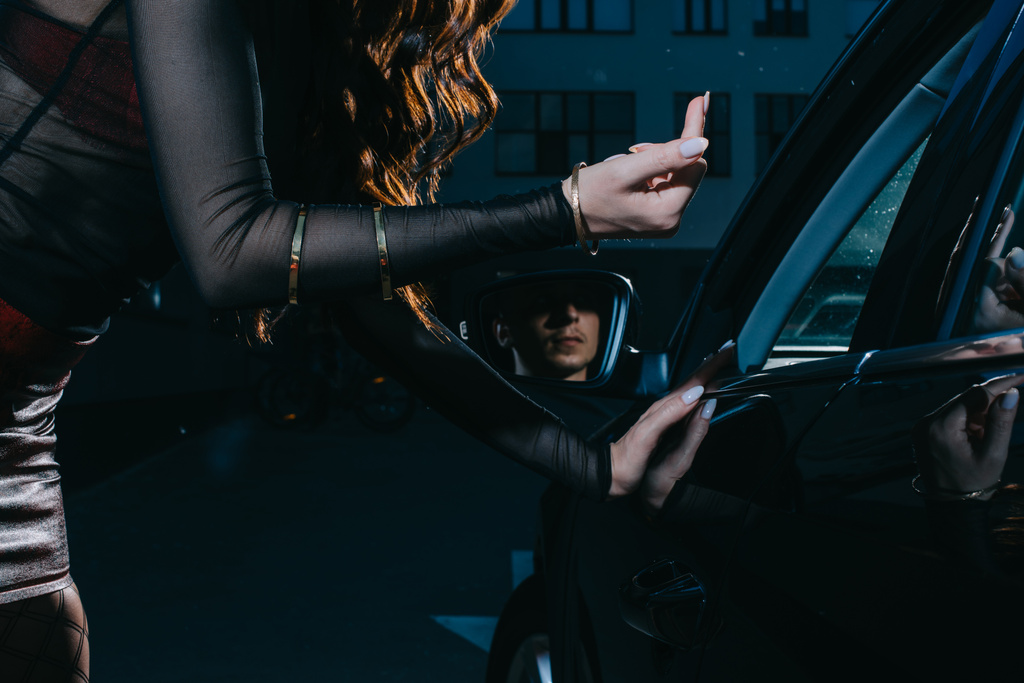 Ausgeschnittener Blick auf Prostituierte, die in Auto neben Mann gestikuliert  - Foto, Bild