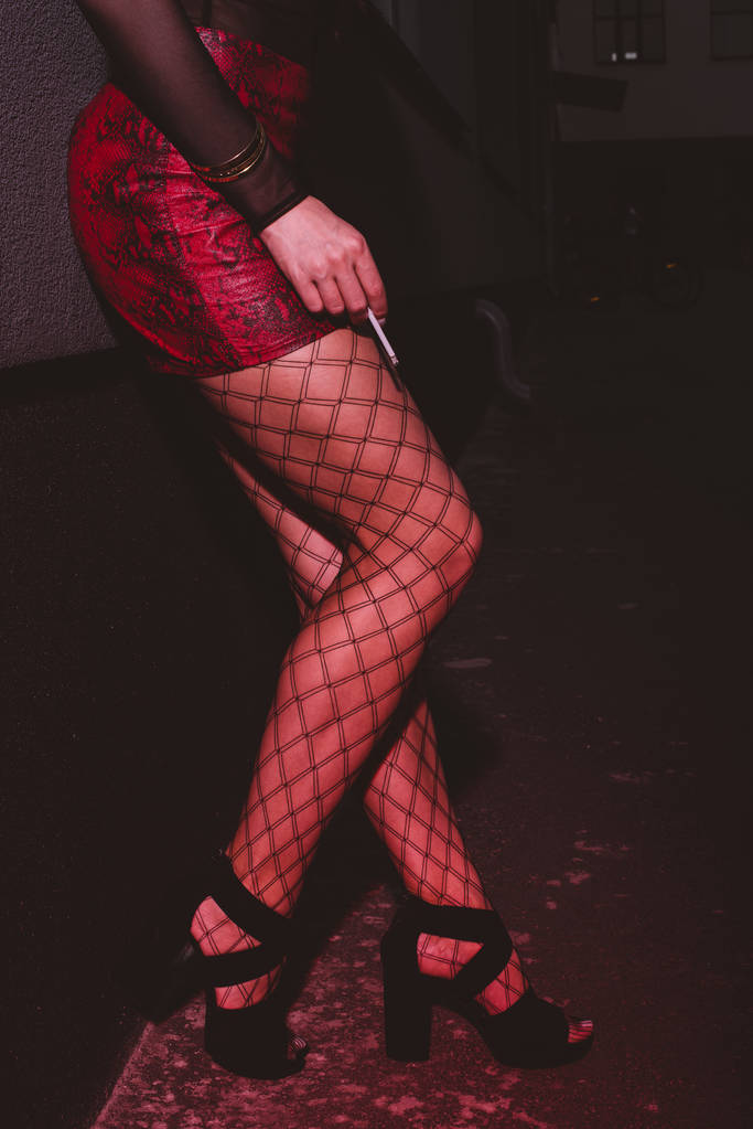 duvar ayanında duran ve sigara tutan kırmızı etekli kadın kırpılmış görünümü  - Fotoğraf, Görsel