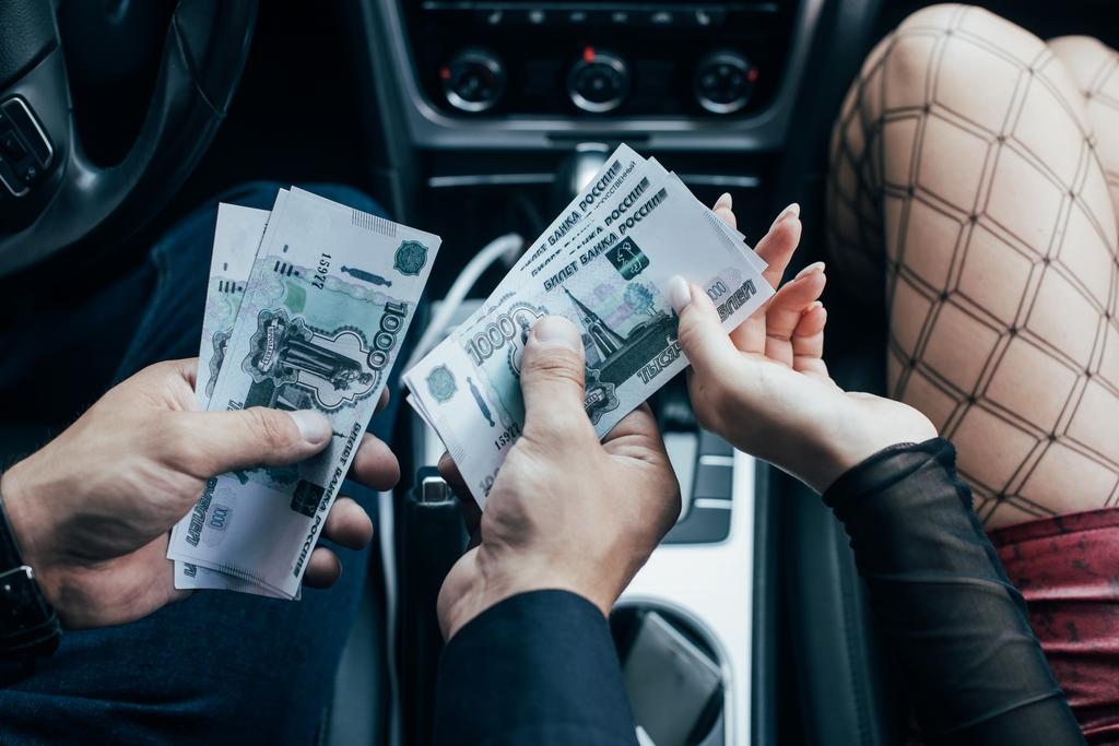 bijgesneden weergave van klant geld betalen aan prostituee in auto  - Foto, afbeelding