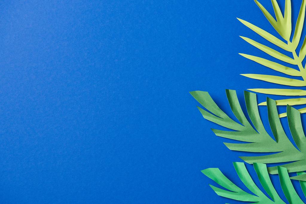 top view of green paper cut exotic leaves on blue background with copy space - Photo, Image